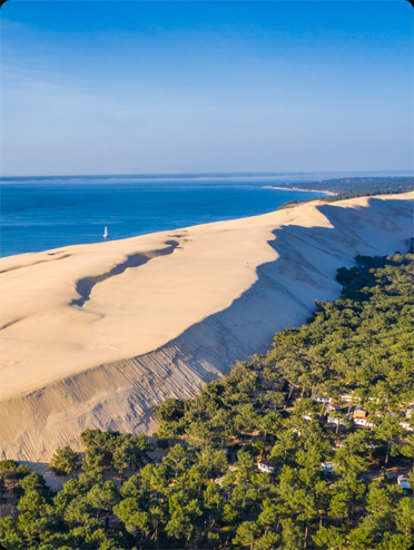 Vue aérienne du Camping au pied de la Dune du Pilat bordée par la forêt de pins et l'océan Atlantique en arrière-plan.