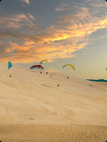 Parapentistes au départ de la Dune du Pilat avec un ciel coloré par le coucher du soleil.